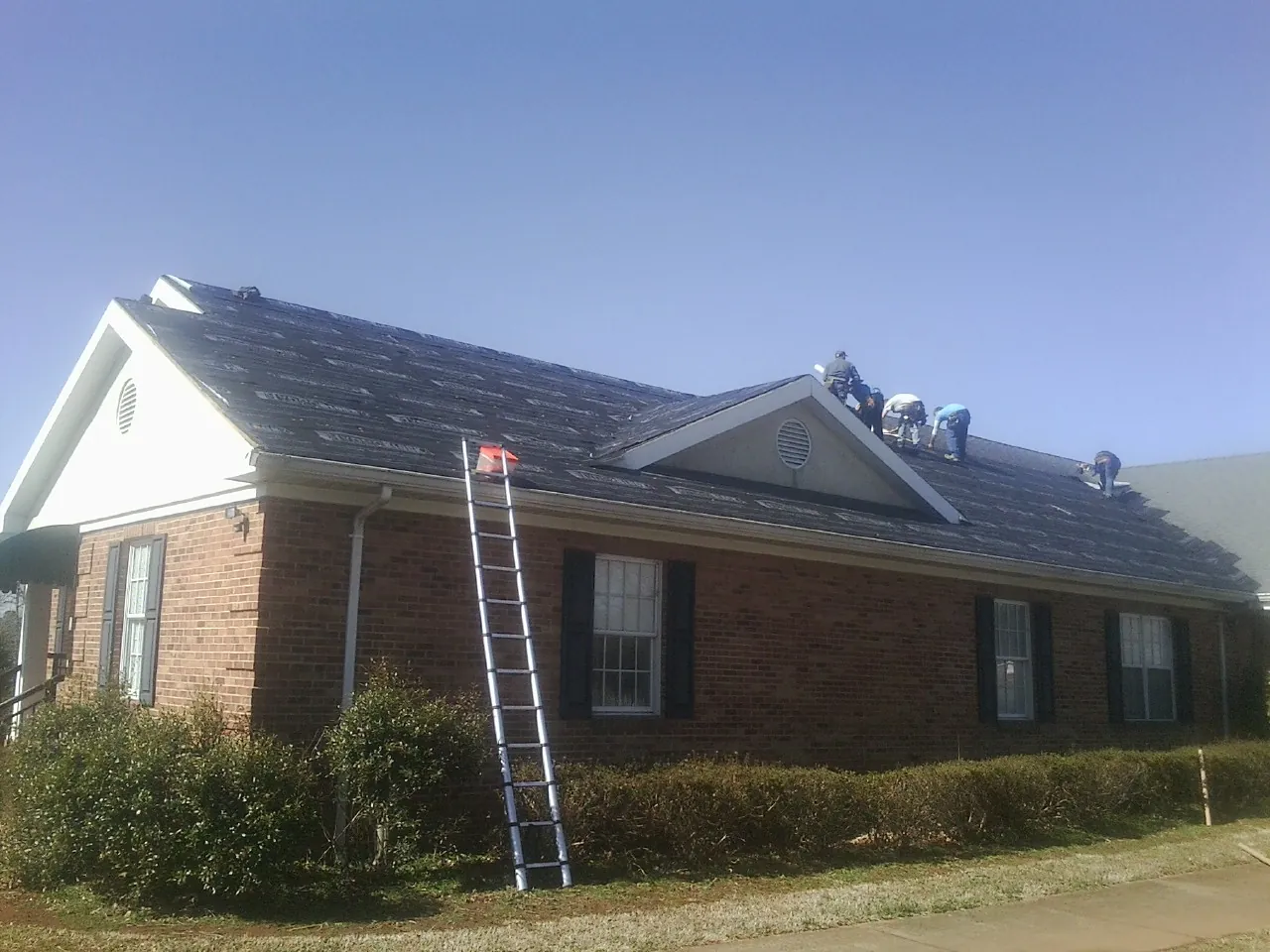 Crew tearing shingles off a brick ranch roof with a ladder set — Emergency Roof Repair work by our crew in Price