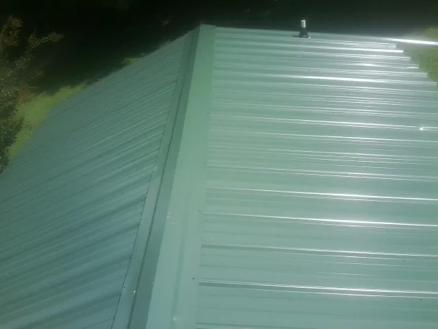New green metal panels meeting at the ridge of a roof — Flat Roof Repair work by our crew in Price