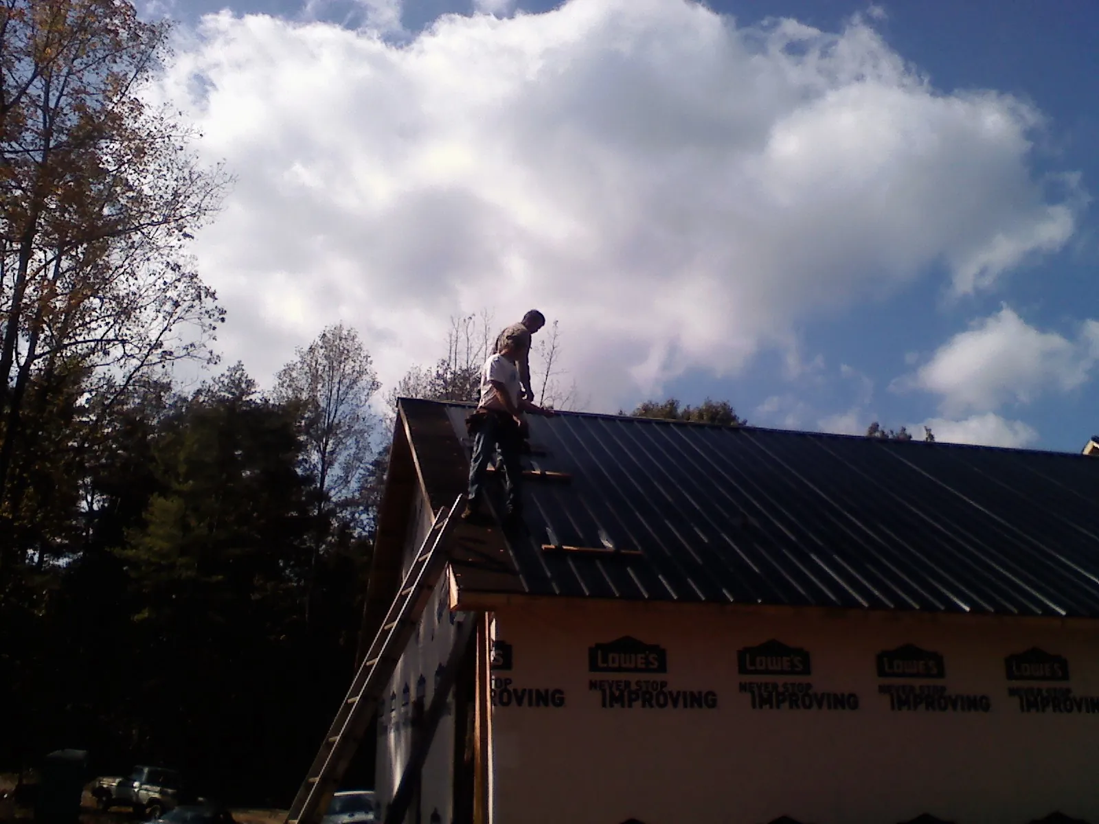 Roofer fastening dark metal panels high against a cloudy sky, from a Roof Inspection job in Price