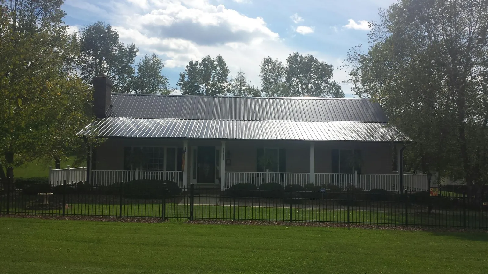 Gray metal roof on a brick ranch with a full width front porch — Gutter Guard Installation work by our crew in Price