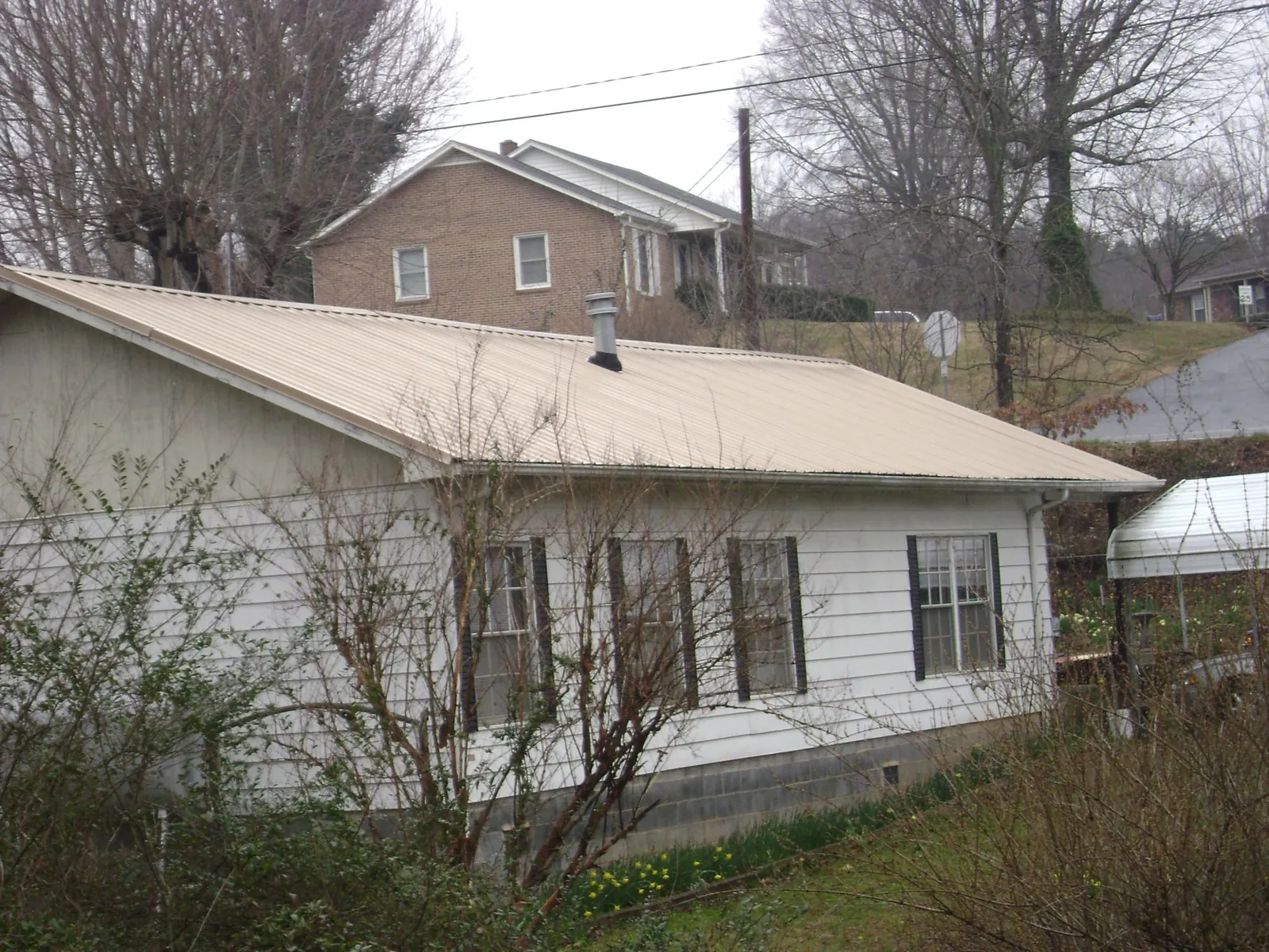 Tan metal roof on a white sided house set into a hillside — Commercial Roofing by Roofing Brothers in Price
